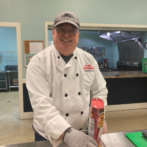 A man wearing a white chef's jacket while smiling at the camera in a kitchen